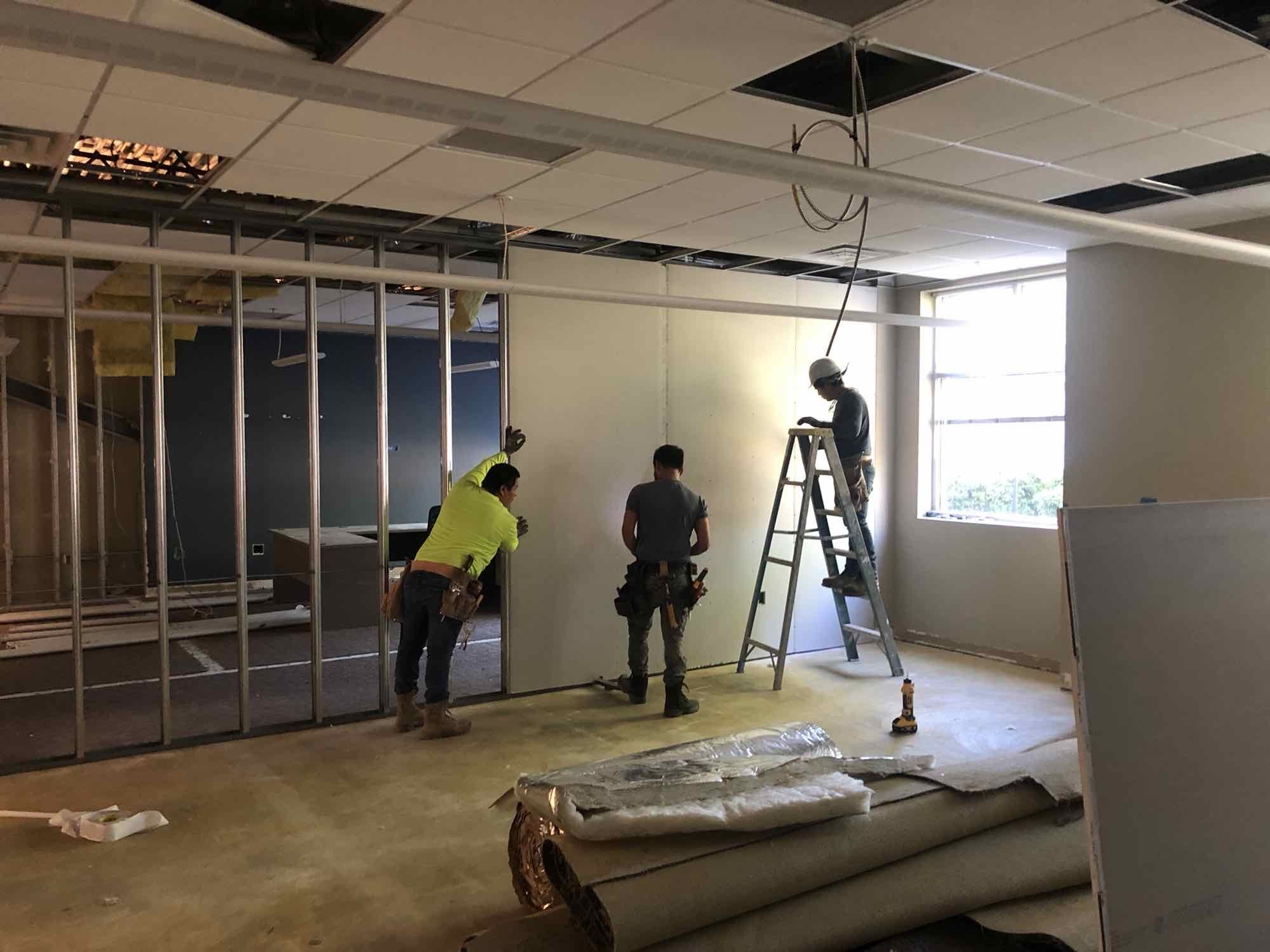 Three construction workers putting up drywall.